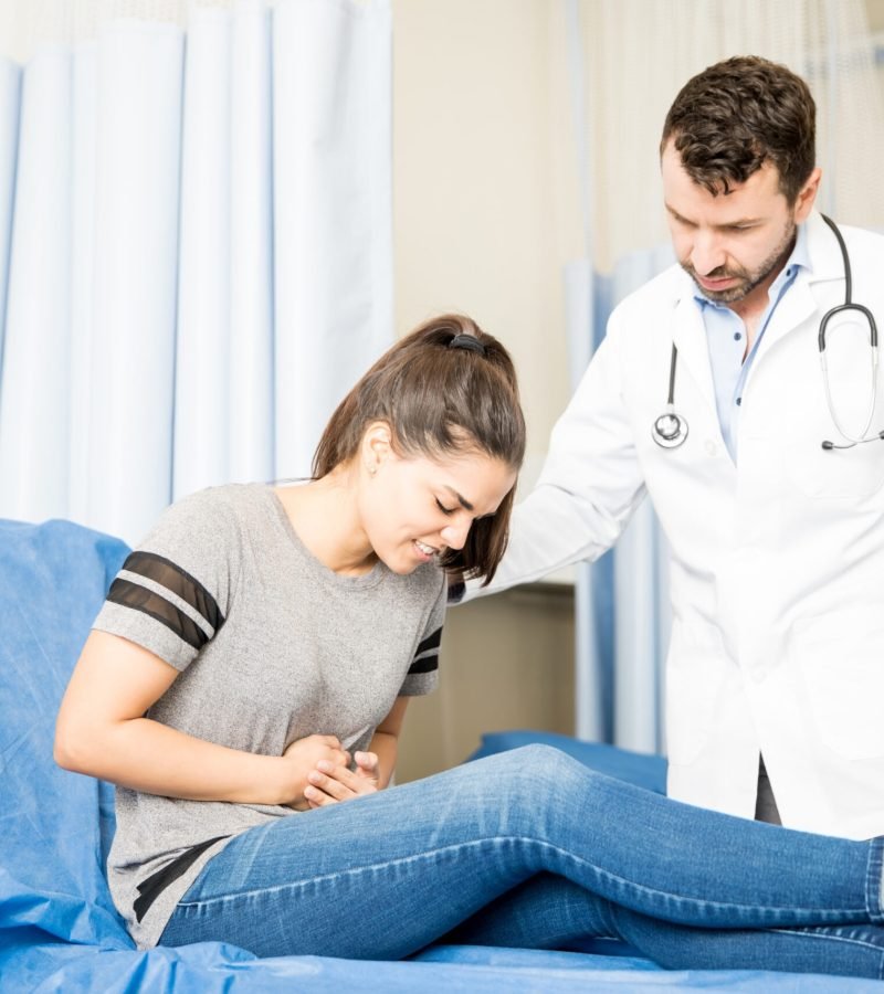Woman with stomach ache visiting doctor Beautiful young woman having severe stomach ache visiting doctor for treatment